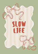 Rode Slow life letters en twee rode lintstrikken op beige strepen binnen een witte golfrand op groen.