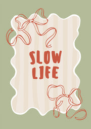 Rode Slow life letters en twee rode lintstrikken op beige strepen binnen een witte golfrand op groen.