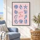 Meet Me by the Sea – Blauwe Schelpen op Roze in een zonnig strandhuis met witte houten wand, zachtblauwe fauteuil, rieten bijzettafel en dunne zwarte lijst