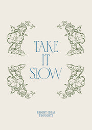 Take It Slow – Groene Bloemen en Blauwe Letters – Groene bloemen omlijsten blauwe Take It Slow letters op een lichte achtergrond.