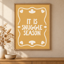 Snuggle Season in een houten lijst boven een eiken kast in een warm beige interieur